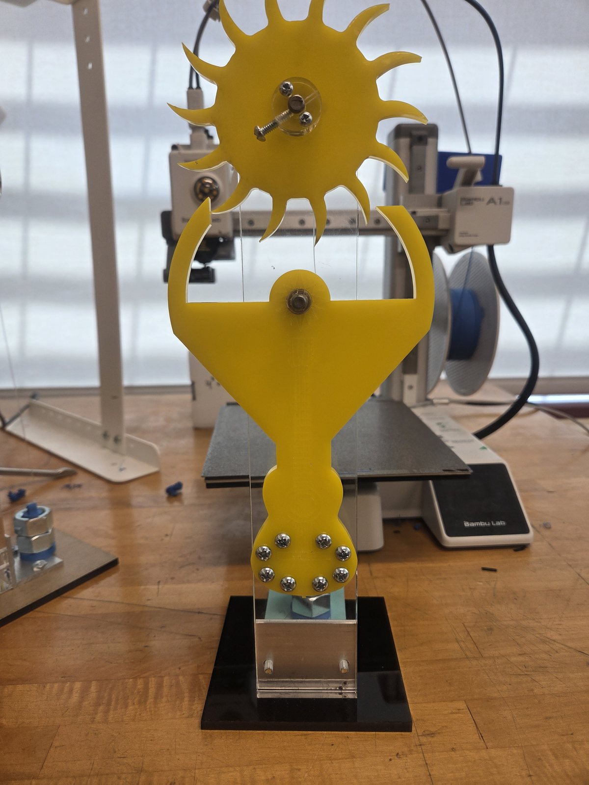 A yellow kinetic sculpture prototype with a sun-shaped gear